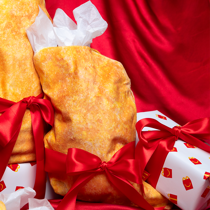 McNugget Stocking with red ribbons on a red fabric background alongside Happy Meal Gift Wrapped presents