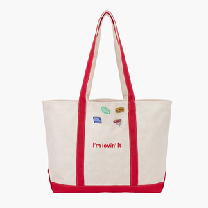 Front view of canvas tote bag with red trim and red handles, featuring the text "i'm lovin' it" printed in red across the centre, decorated with McDonaldland Pins (sold seperately)