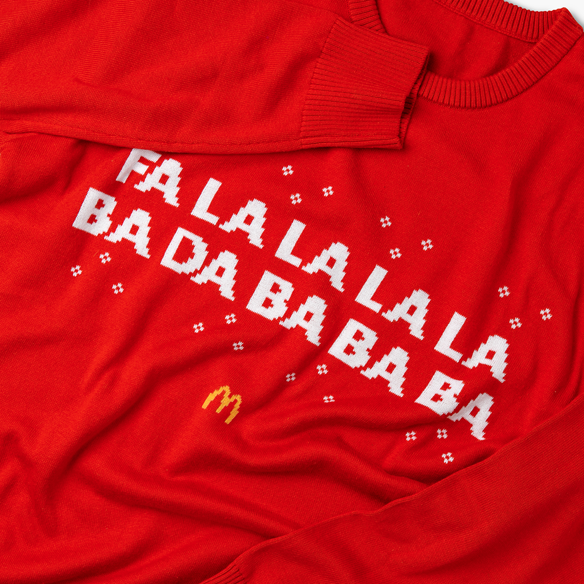 Close-up of ribbed cuff and collar with pixel-style “Fa La La La…” text, snowflake accents, and McDonald’s Golden Arches logo beneath. 