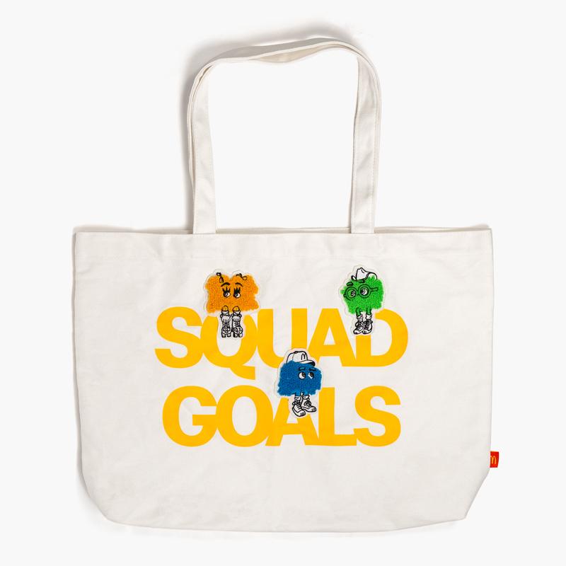 off-white tote bag with mustard-yellow writing in all caps titled "SQUAD GOALS" with three fry kids perched on the letters