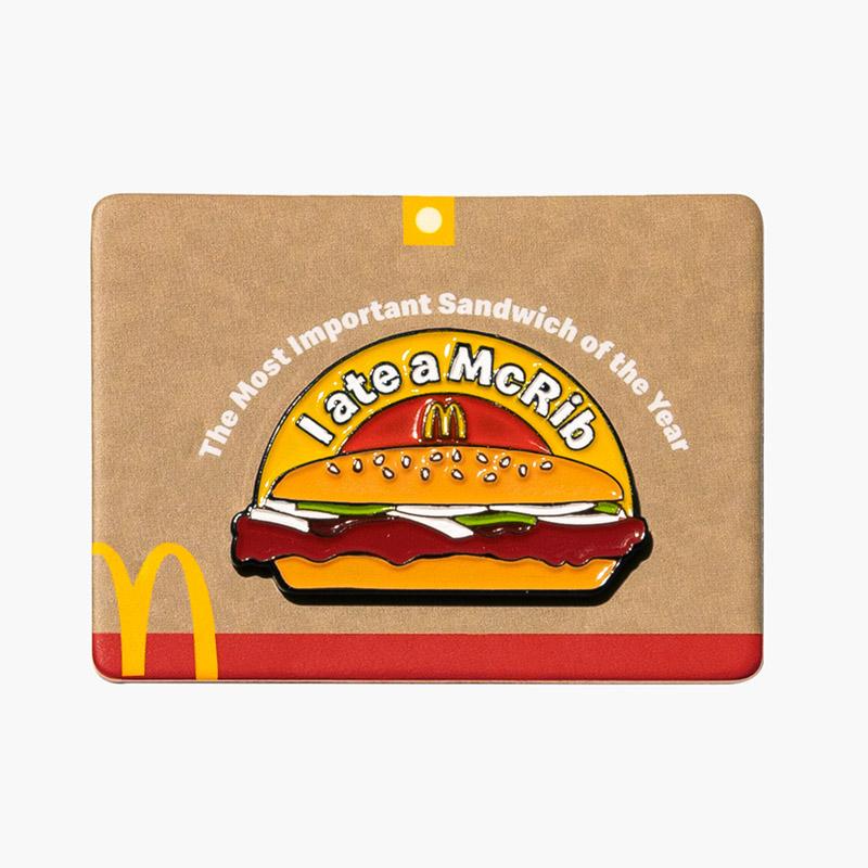 brown rectangle pin with McDonald's golden arches in the bottom left corner and a McRib sandwich   in the middle with a banner above it that says "The Most Important Sandwich of the Year" and beneath it, "I Ate a McRib"